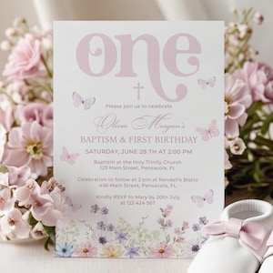 May include: A pink and white invitation card for a baptism and first birthday celebration. The card features the word "one" in large letters, butterflies, and floral accents. Two pairs of white baby shoes with pink bows are in the foreground.