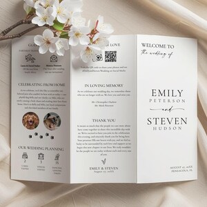 Op de afbeelding: Een drievoudige trouwuitnodiging met de namen "Emily Peterson en Steven Hudson" in elegant schrift. De uitnodiging bevat secties voor huwelijksdetails, een bedankbericht en een QR-code. Witte bloemen en een tak op de achtergrond.