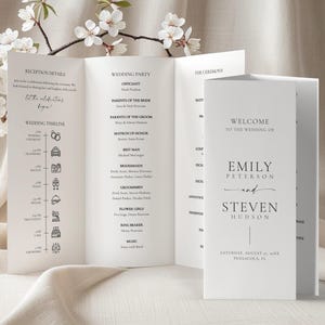 May include: A white wedding program, folded into a tri-fold design, with elegant black text. The program includes the wedding party details, timeline, and a welcome message for Emily Peterson and Steven Hudson.
