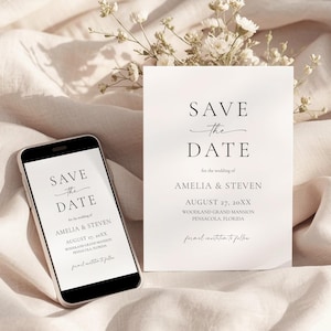 May include: A smartphone and a white card with the text "Save the Date" in elegant black script. The card includes the names Amelia & Steven, the date August 27, and the location. Delicate white flowers are in the background.