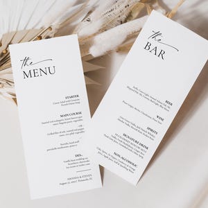 Può includere: Due biglietti di menu bianchi con testo nero. Uno dice "The MENU" ed elenca i piatti. L'altro dice "The BAR" ed elenca le bevande. Accenti floreali secchi sono sullo sfondo. Il menu include i nomi degli sposi.