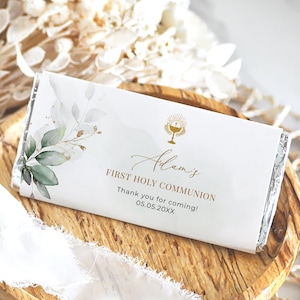 Puede incluir: Una barra de chocolate blanco envuelta en papel de aluminio plateado con una etiqueta personalizada. La etiqueta presenta un cáliz dorado con una cruz, hojas de acuarela verde y dorado, y el texto "Adam's First Holy Communion Thank you for coming! 05.05.20XX".