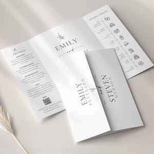 May include: Elegant white wedding invitation suite with the names "Emily" and "Steven" printed in a stylish font. The suite includes a timeline, details, and RSVP information. The design is minimalist and modern, perfect for a wedding.