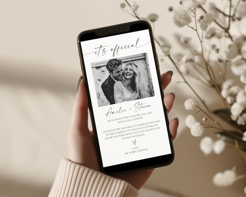 May include: A smartphone displays a wedding announcement. The black and white photo shows a smiling couple. The text reads "its official" and includes the names "Amelia + Steven" and wedding details. The phone is held in a hand.