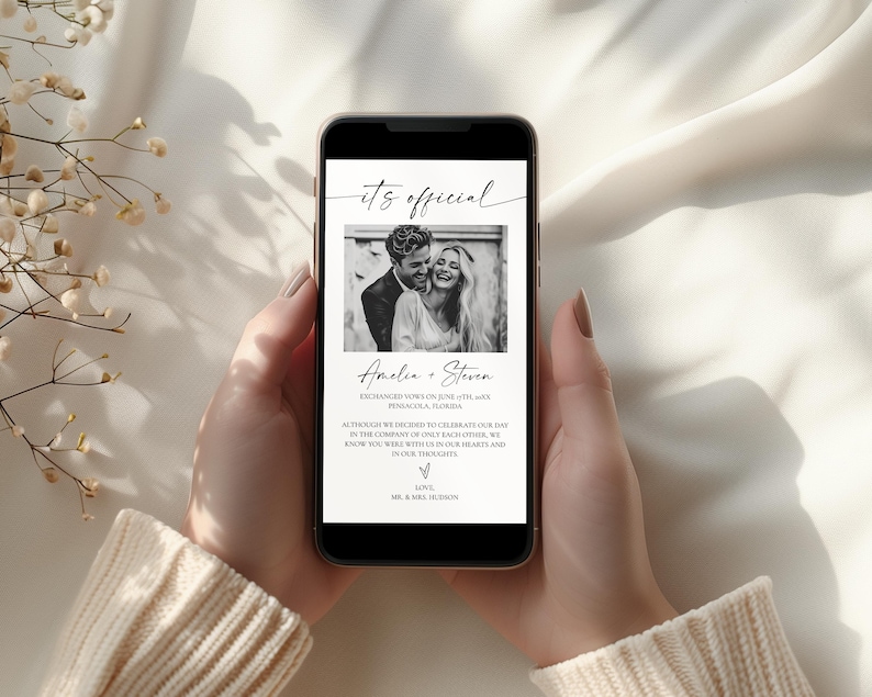 May include: A smartphone displays a wedding announcement. The screen shows a black and white photo of a couple, with the words "it's official" at the top. The announcement includes the couple's names and a message.