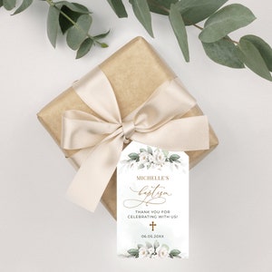 May include: White floral baptism favor tag with gold lettering. The tag says "Michelle's Baptism" and "Thank you for celebrating with us!" with a gold cross and the date "06.05.20XX".