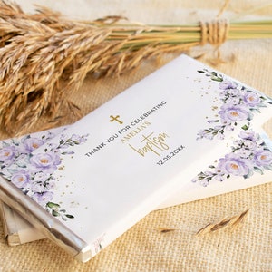 Puede incluir: Barra de chocolate blanco envuelta en papel blanco con un diseño floral morado y detalles dorados. El texto "Thank you for celebrating Amelia's Baptism 12.05.20XX" está impreso en el envoltorio.