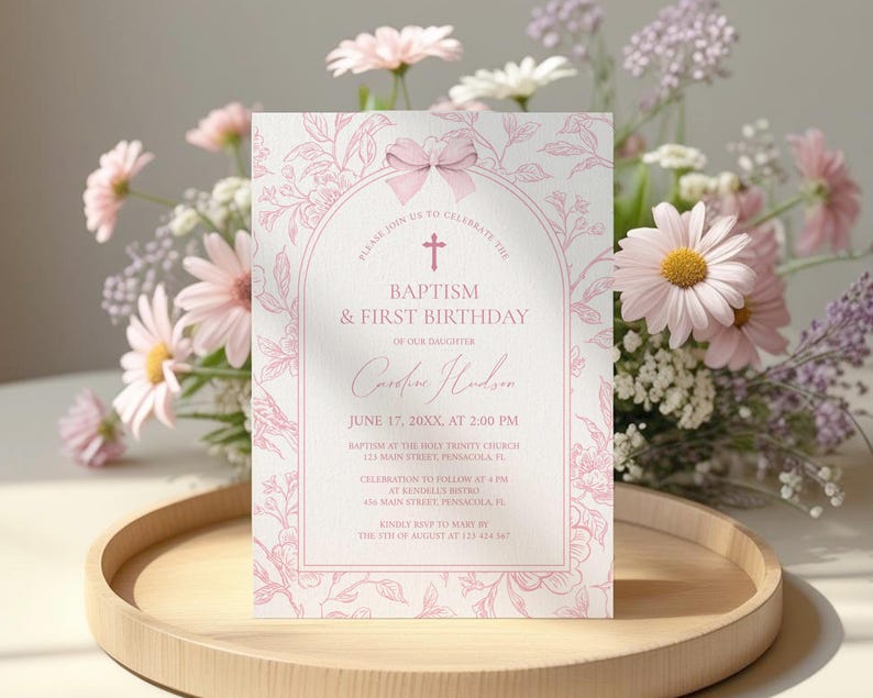 May include: A pink and white invitation card for a baptism and first birthday celebration. The card features floral illustrations and the text "Baptism & First Birthday" with event details. The card is displayed on a wooden tray with a floral arrangement.