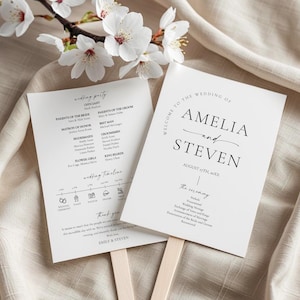 May include: Two white wedding fans with black text, one listing the wedding party and timeline, the other welcoming guests to Amelia and Steven's wedding. Cherry blossoms and a beige fabric background.
