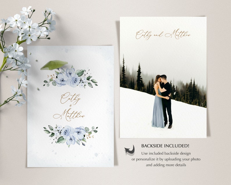 May include: A wedding invitation with a watercolor design featuring blue flowers and greenery. The invitation reads "Cathy & Matthew" in gold script. The back of the invitation features a photo of a couple in a snowy forest.