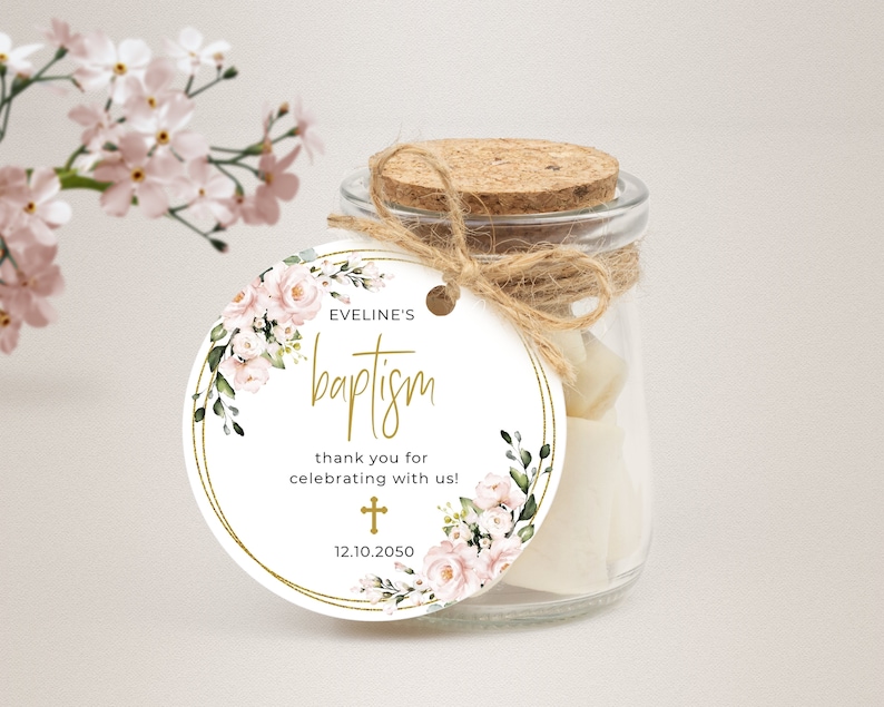 Może przedstawiać: Okrągła biała etykieta z złotą obw&oacute;dką i kwiatowym wzorem. Tekst na etykiecie brzmi "Eveline's Baptism" i "thank you for celebrating with us!" z małym krzyżem i datą "12.10.2050".