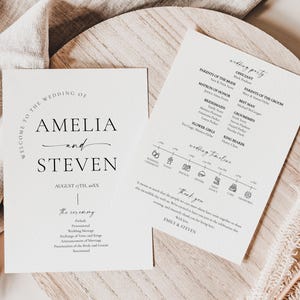 May include: Two wedding stationery cards with elegant typography. One card reads "Welcome to the Wedding of Amelia and Steven" with the date. The other card lists the wedding party and timeline. The cards are on a wooden surface.