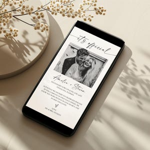May include: A smartphone displays a wedding announcement with a black and white photo of a couple. The text reads "it's official" and includes the names Amelia and Steven, along with a message and the words "Love, Mr. & Mrs. Hudson."
