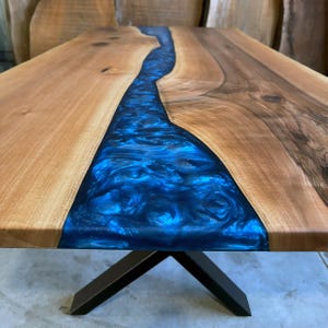 May include: A wooden table top with a blue epoxy resin river running through the center. The table has a black metal X-shaped base.