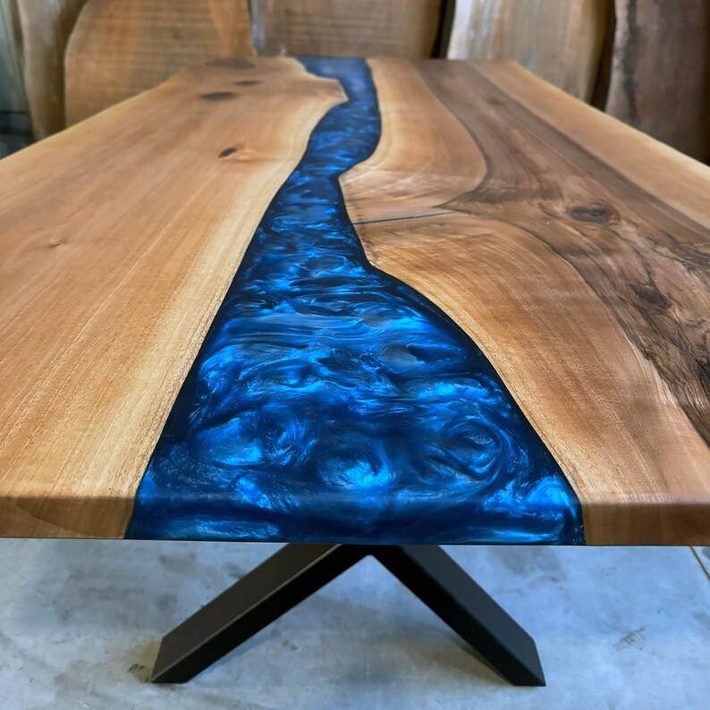 May include: A wooden table top with a blue epoxy resin river running through the center. The table has a black metal X-shaped base.