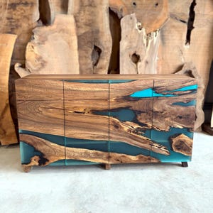 May include: A handcrafted wooden cabinet with a unique design. The cabinet features a natural wood grain finish with sections of vibrant turquoise resin. The doors and sides showcase the contrast between the wood and resin, creating a striking visual effect.