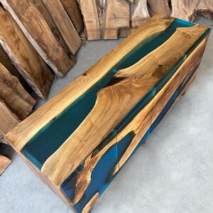 May include: A wooden console table with two drawers features a unique design with a blue resin river flowing through the wood grain.