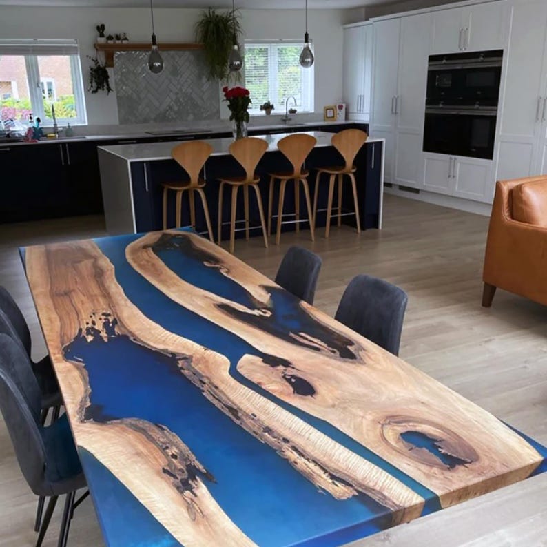 Puede incluir: Una gran mesa de comedor de madera con un r&iacute;o de resina epoxi azul que atraviesa el centro. La mesa est&aacute; rodeada de sillas y se encuentra en una cocina moderna.