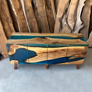 May include: A wooden cabinet with three doors and a blue resin top. The cabinet has a natural wood finish and the resin is a deep blue color. The cabinet is sitting on a concrete floor.