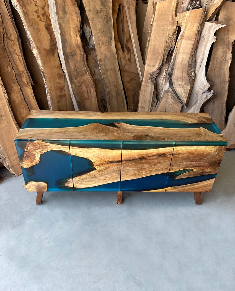 May include: A wooden cabinet with three doors and a blue resin top. The cabinet has a natural wood finish and the resin is a deep blue color. The cabinet is sitting on a concrete floor.