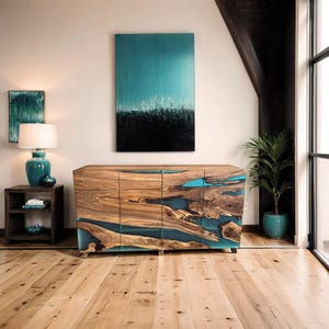 Peut inclure: Un buffet en bois avec trois portes et un incrustation de résine époxy bleu turquoise. Le buffet a une finition en bois naturel et est posé sur un sol en bois. Il y a une peinture sur le mur derrière le buffet.