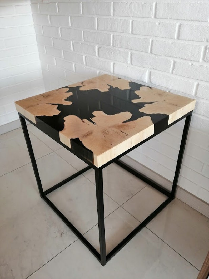 K&ouml;nnte beinhalten: Ein quadratischer Holztisch mit einer schwarzen Epoxidharzeinlage. Der Tisch hat einen schwarzen Metallrahmen.