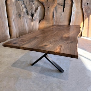 May include: A large, dark brown wooden dining table with a live edge top and a black metal X-shaped base.