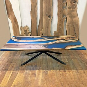 Puede incluir: Una mesa de madera grande con una tapa de resina epoxi azul. La mesa tiene una veta de madera natural y una base de metal negro.
