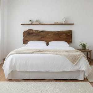 Puede incluir: Una habitación con una cama con cabecero de madera natural. La cama tiene ropa de cama blanca y una manta beige. Una pequeña mesita de noche de madera sostiene una planta. Una estantería sobre la cama exhibe objetos decorativos.