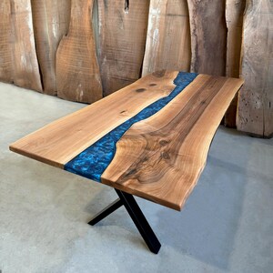 May include: A live edge walnut dining table with a blue epoxy river running through the center. The table has a black metal X-shaped base.