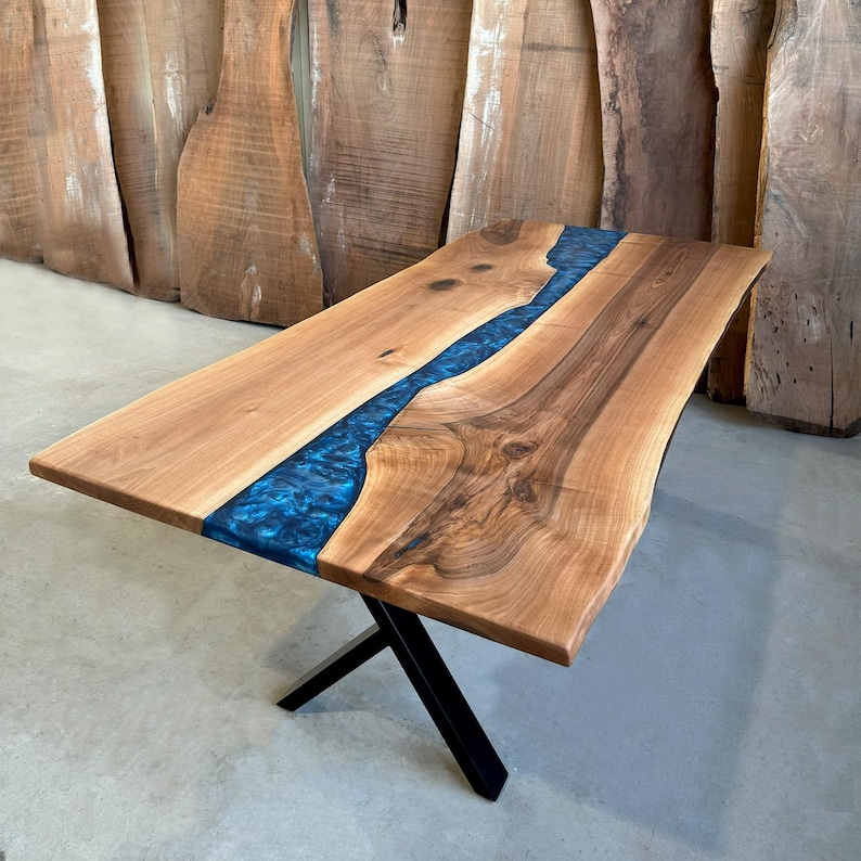 May include: A live edge walnut dining table with a blue epoxy river running through the center. The table has a black metal X-shaped base.