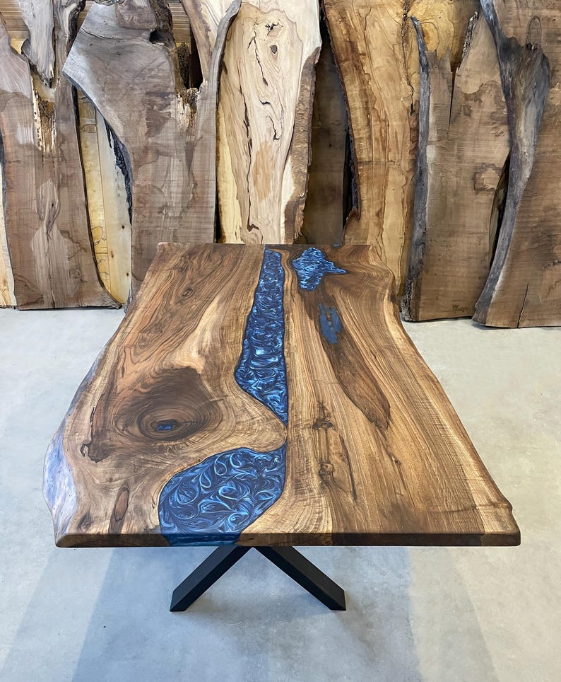 May include: A large wooden table with a blue resin inlay. The table has a live edge and a black X-shaped base.