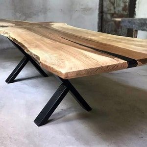 May include: A large wooden table with a live edge top and black metal X-shaped legs. The table top has a natural wood grain and a black epoxy resin inlay.