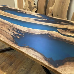 Puede incluir: Una mesa de madera con una incrustaci&oacute;n de resina epoxi azul. La resina fluye en un patr&oacute;n de r&iacute;o a trav&eacute;s de la madera.