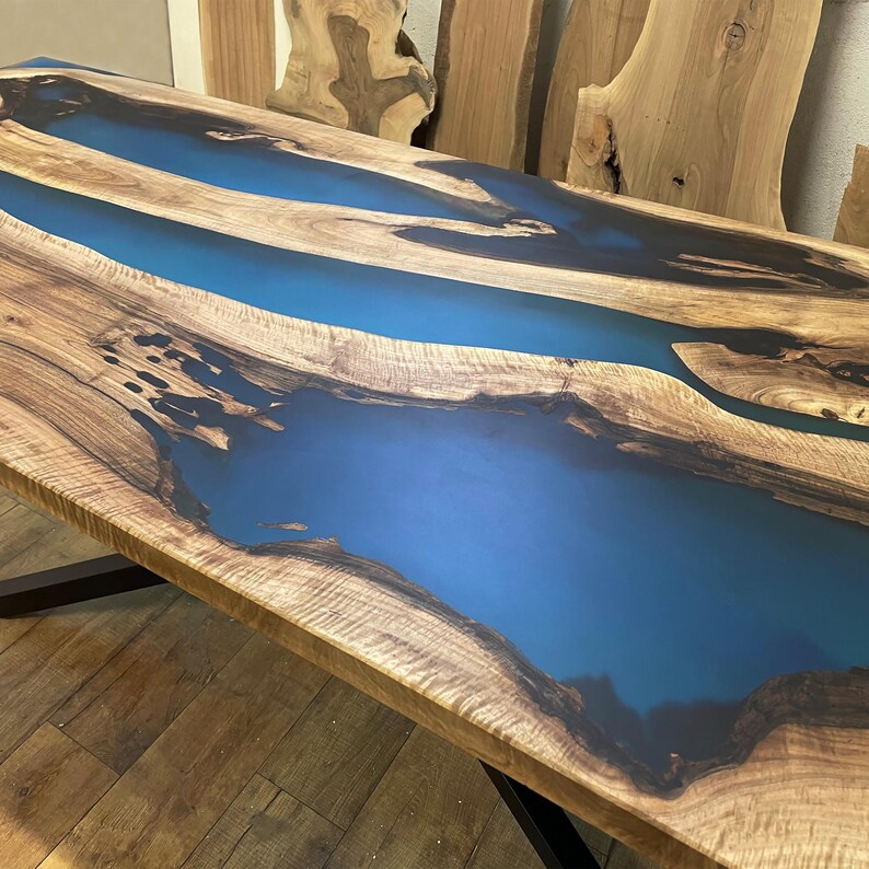 Puede incluir: Una mesa de madera con una incrustaci&oacute;n de resina epoxi azul. La resina fluye en un patr&oacute;n de r&iacute;o a trav&eacute;s de la madera.