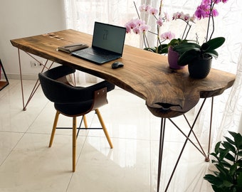 Può includere: Una scrivania in legno con un piano in legno vivo e gambe a forcina in metallo. Un computer portatile, un taccuino e un mouse sono sulla scrivania. Ci sono due piante di orchidea in vaso sullo sfondo.