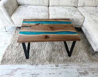 Puede incluir: Una mesa de centro de madera con una incrustación de resina epoxi turquesa. La mesa tiene un marco de metal negro y está sobre una alfombra blanca.