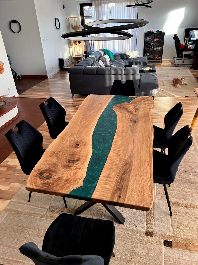 May include: A large wooden dining table with a green epoxy river running through the center. The table has a natural wood finish and is surrounded by black chairs.