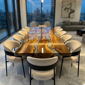 Puede incluir: Una gran mesa de comedor rectangular de madera con un diseño único de resina epoxi, rodeada de doce sillas color crema con detalles en negro. La superficie de la mesa presenta una mezcla de tonos marrones, dorados y plateados. La habitación tiene grandes ventanales con vistas a la ciudad.