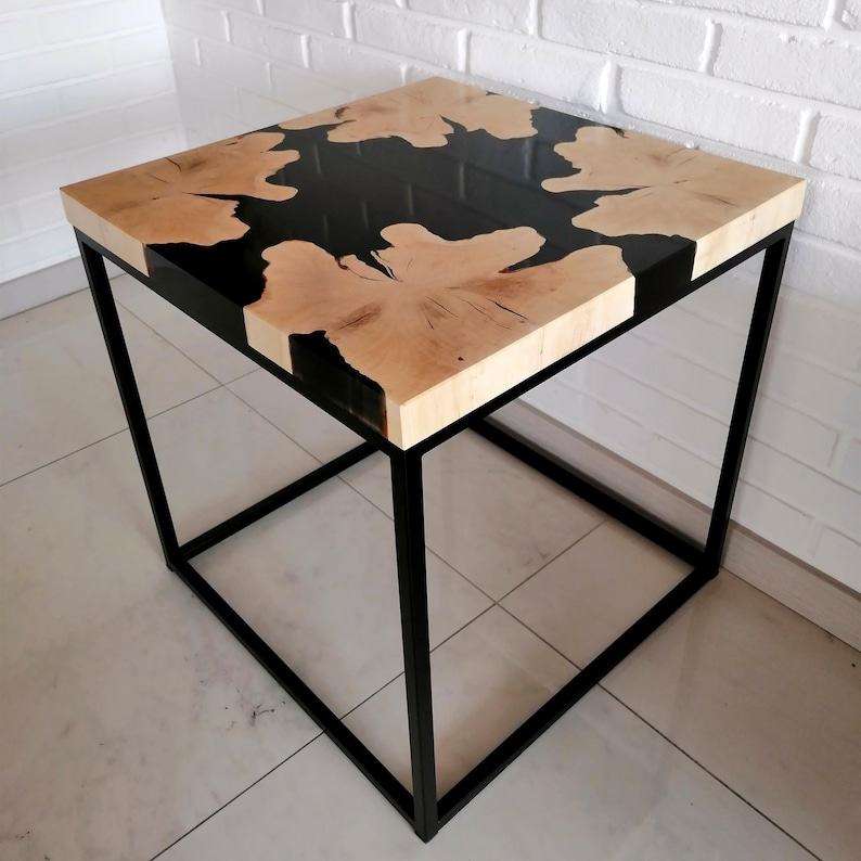 K&ouml;nnte beinhalten: Ein quadratischer Beistelltisch mit einer Tischplatte aus schwarzem Epoxidharz und Holz sowie einem schwarzen Metallgestell.