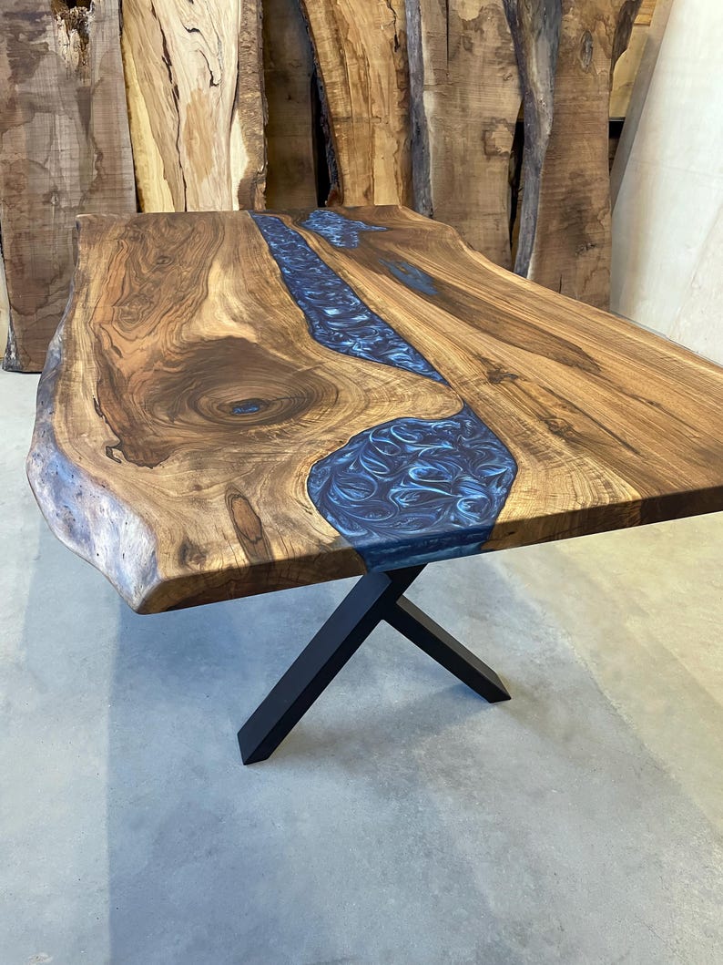 May include: A large wooden table with a live edge top and a blue resin inlay. The table has a black metal X-shaped base.