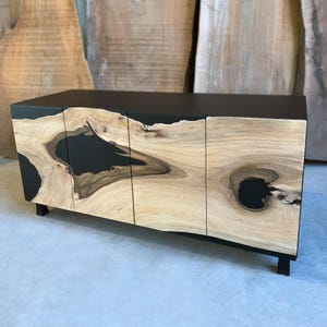 May include: A black and wood cabinet with three doors. The doors are made of wood with black epoxy resin filling in the natural knots. The cabinet has a modern design and would be a great addition to any home.