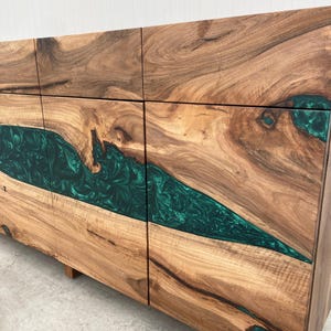 May include: A wooden cabinet with four doors, featuring a green epoxy resin inlay that resembles a river flowing through the wood. The cabinet has a natural wood finish and is made of solid wood.