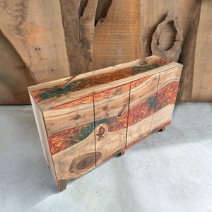 Könnte beinhalten: Ein dreitüriger Holzschrank mit einer gewölbten Oberseite und einer bunten Harzeinlage. Die Einlage zeigt Wirbel in Orange, Rot und Grün.