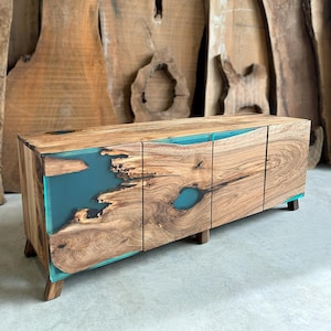 May include: A wooden cabinet with three doors and teal blue resin accents. The cabinet has a natural wood finish and sits on four legs.