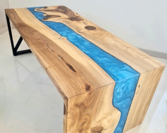 Puede incluir: Una mesa de madera con un río de resina azul que recorre el centro. La mesa tiene un diseño moderno con una base de metal negro.