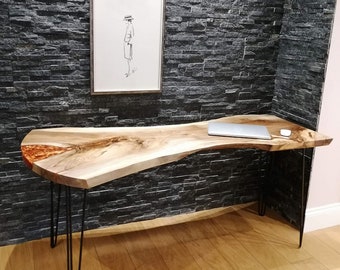 Può includere: Una scrivania con bordo vivo con un piano in legno naturale e un'intarsio in resina epossidica trasparente. La scrivania ha gambe a forcina nere e si trova su un pavimento in legno. Un computer portatile è sulla scrivania.