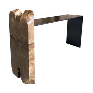 May include: A modern console table with a unique, natural wood base and a black metal top. The wood base has a rustic, organic shape and the metal top is sleek and contemporary.