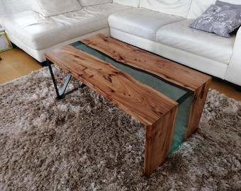 May include: A wooden coffee table with a clear epoxy river running through the center. The table has a natural wood finish and black metal legs.
