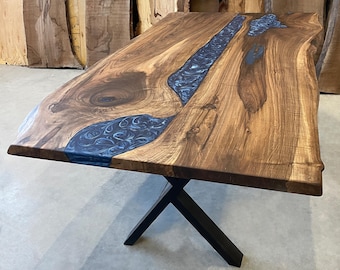 Puede incluir: Una mesa de madera grande con una tapa de borde vivo y un río de epoxi azul que atraviesa el centro. La mesa está sostenida por una base de metal negro en forma de X.